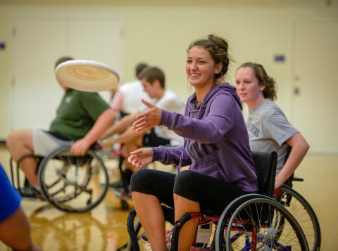 Student in wheelchair smiles while throwing frisbee