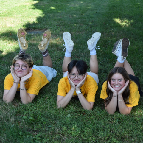 Three CONNECT student laying on the grass in yellow t shirts