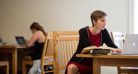 UNH student sitting at desk in library with books and laptop