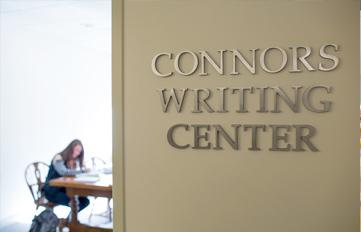 UNH Connors Writing Center sign with student reading book in distance