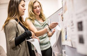 Two UNH students in classroom looking at publication papers