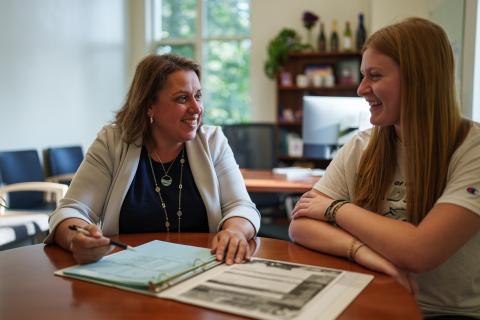 UNH employee sitting at a desk with a student reviewing paperwork