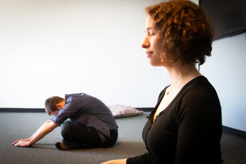Two students meditating, one is sitting upright, the other is in childs pose.