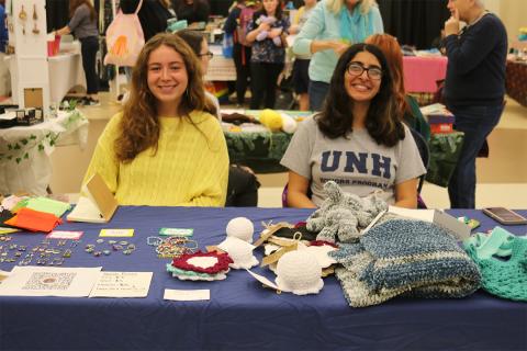 Two students sitting at table with jewelry and crochet crafts.