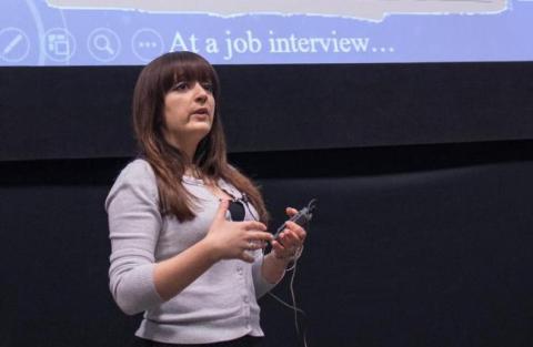Female researcher speaks in front of large screen holding microphone