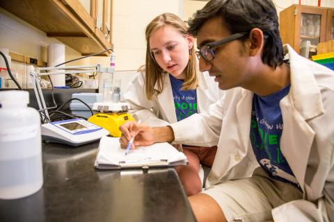 Two researchers wearing white lab coats in a lab reviewing notes