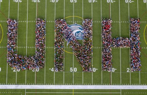 aerial of UNH students standing on football field in UNH pattern