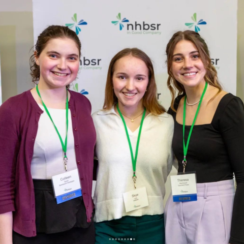 Three people smiling wearing name tags on lanyards with NHBSR logo in the background