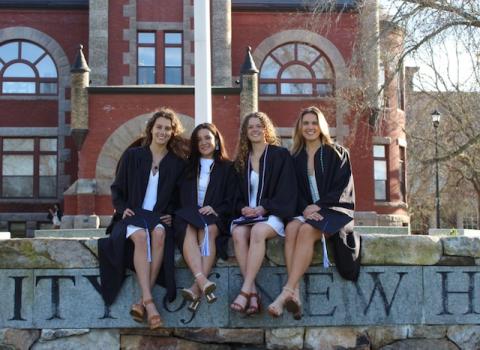 group of four people sitting outside in graduation gowns