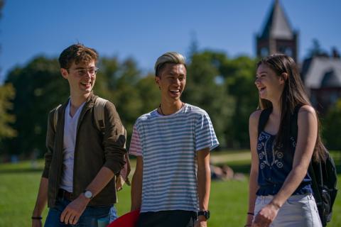 Three students walking and talking with T-Hall in the background