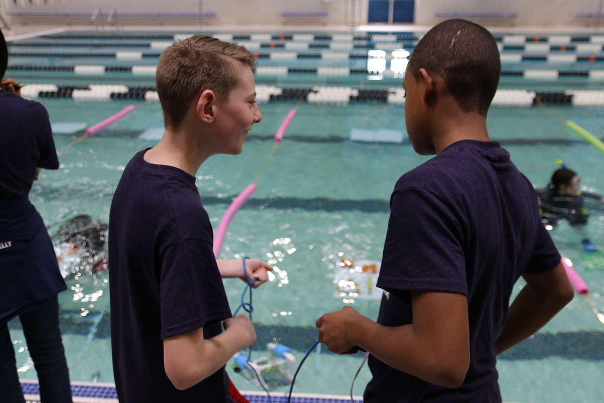 Two New Hampshire middle school students driving their underwater robots at the UNH pool