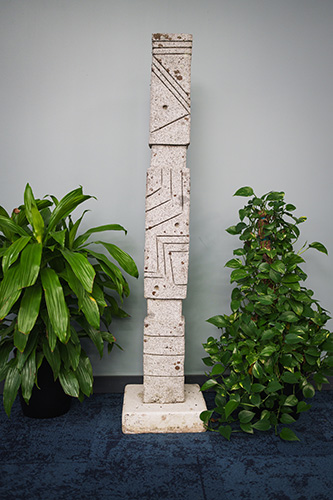 A slender white obelisk between two green plants