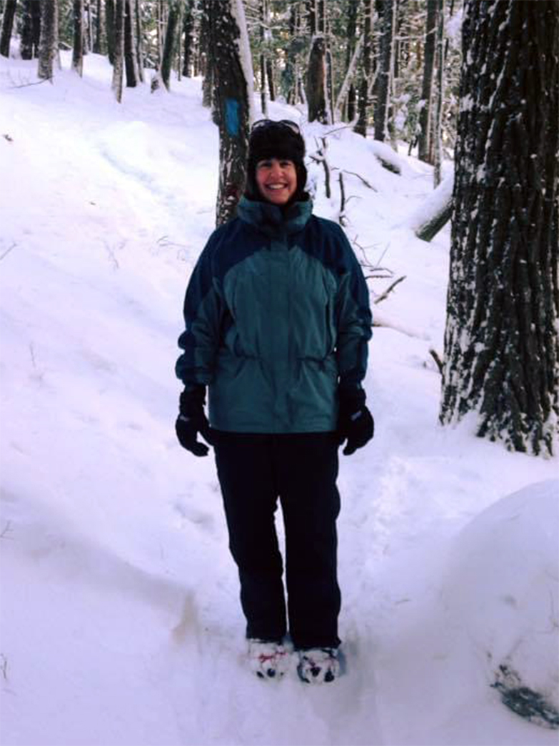 A photo of a woman dressed for the winter and hiking in the woods.