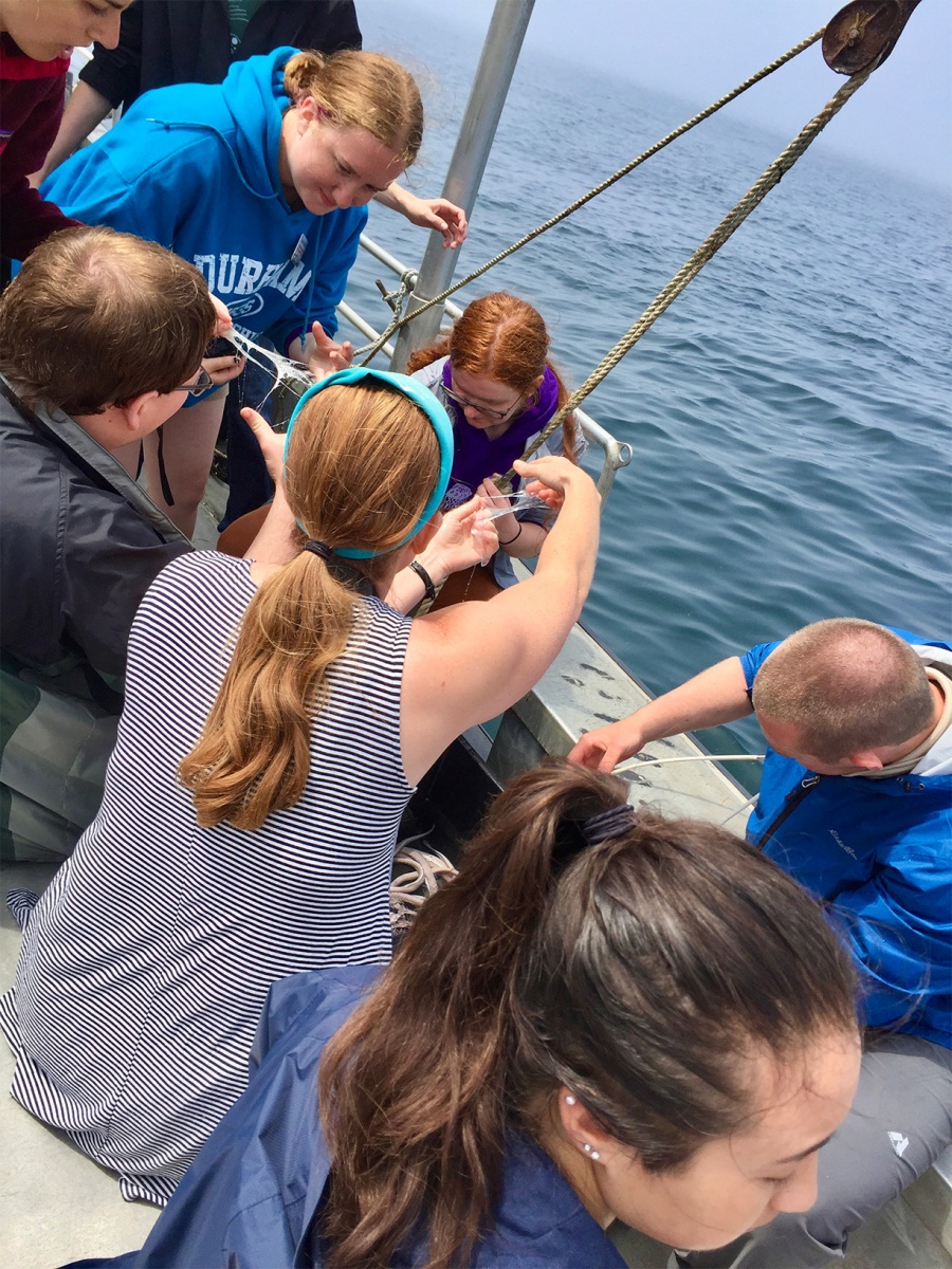 A group of people onboard a boat in a body of water hold up slime, stretching it out.