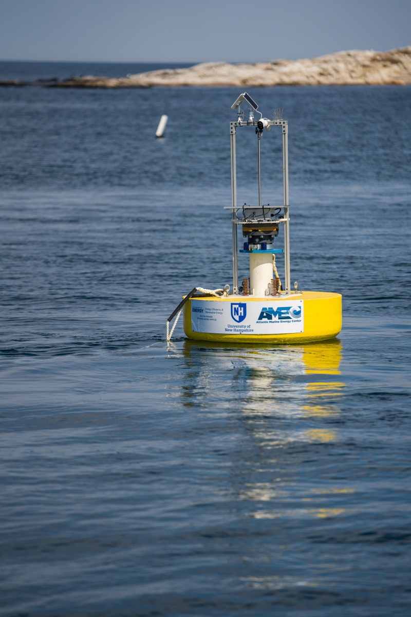 Yellow University of New Hampshire marine energy buoy at sea, with island in background