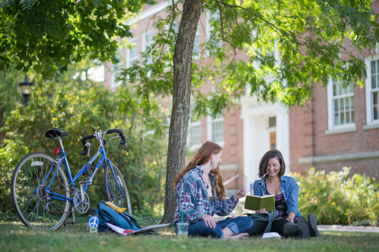 Two women sitting under a tree on a summer day at UNH