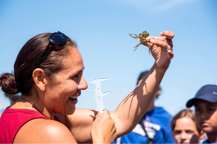 Woman in red shirt holds up a crab and smiles at it