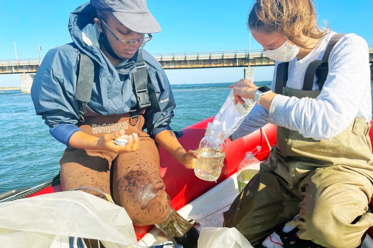 Two researchers sit on a boat looking through samples collecting from the estuary for microplastics.