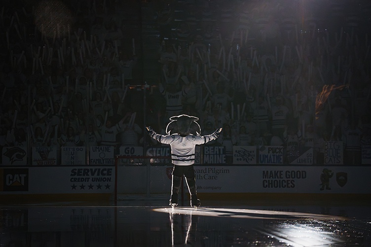 UNH mascot throws his arms out to the side in front of an excited hockey crowd