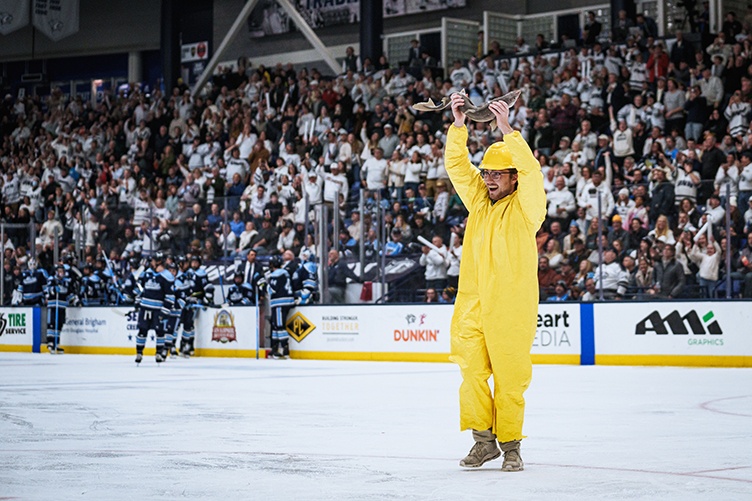 A man holds a fish over his head on the ice at a hockey game