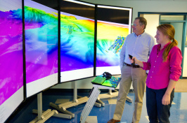 Two researchers in front of a brightly colored screen depicting the seafloor