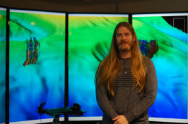 Drew Stevens stands in front of large computer screens.