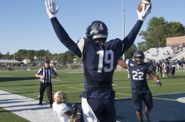 UNH football player holding football in the air