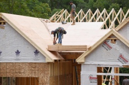 An image of two roofers working on the roof of a house that's under construction.
