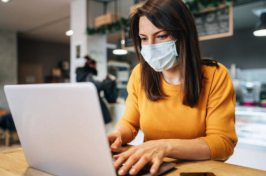 A women wearing a mask sits at a laptop