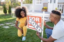 A couple places a "sold" sign  on top of a "for sale" sign in their lawn.