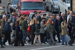 A large group of people cross a busy city street.