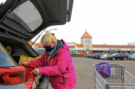 An elderly woman loads groceries into her trunk