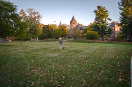 Student walking across lawn, T Hall in the background 