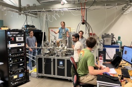 Five people work in a lab full of computers and other equipment