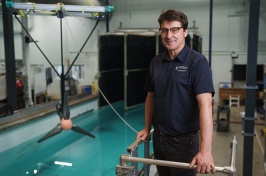 Male researcher stands above engineering test tank with large turbine behind