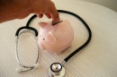 a person putting a coin into a piggy bank which is surrounded by a stethoscope (CREDIT 401(K)2013 / FLICKR)