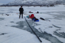 Young man dressed in warm winter clothing stands on frozen lake next to long series of black sediment cores. 