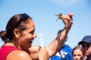 Woman in red shirt holds up a crab and smiles at it