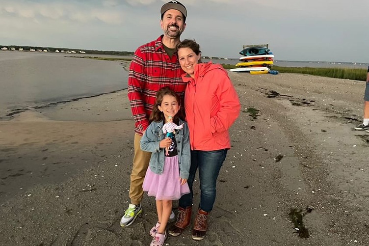 Wife and husband standing on beach with their young daughter in front of them