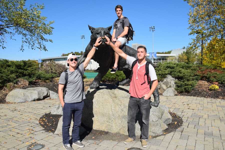Three members of UNH's club lacrosse team pose in front of the wildcat statue 