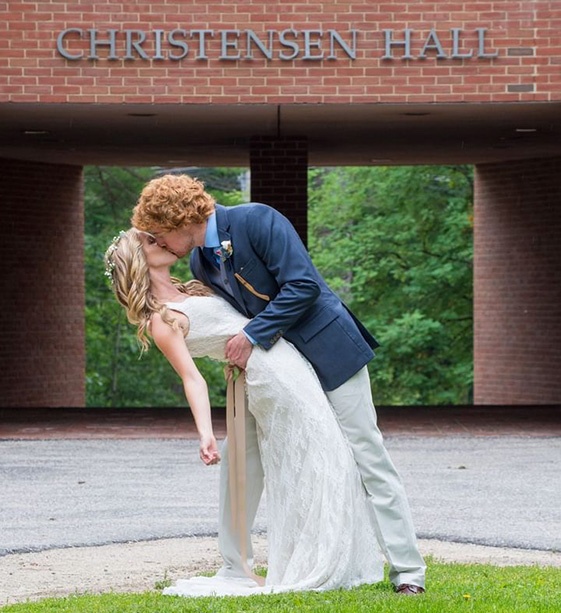 Groom dipping his bride for a kiss in front of university building