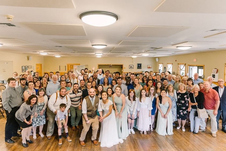 Large group of friends and family pose with bride and groom at wedding reception