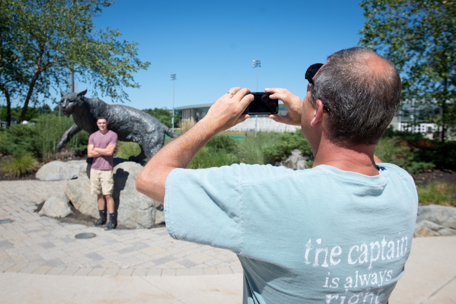 A man takes a picture of a student in front of the wildcat. 