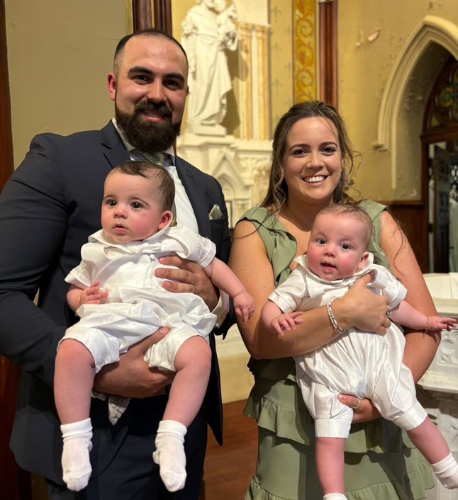 Husband and wife stand next to each other, each holding a baby